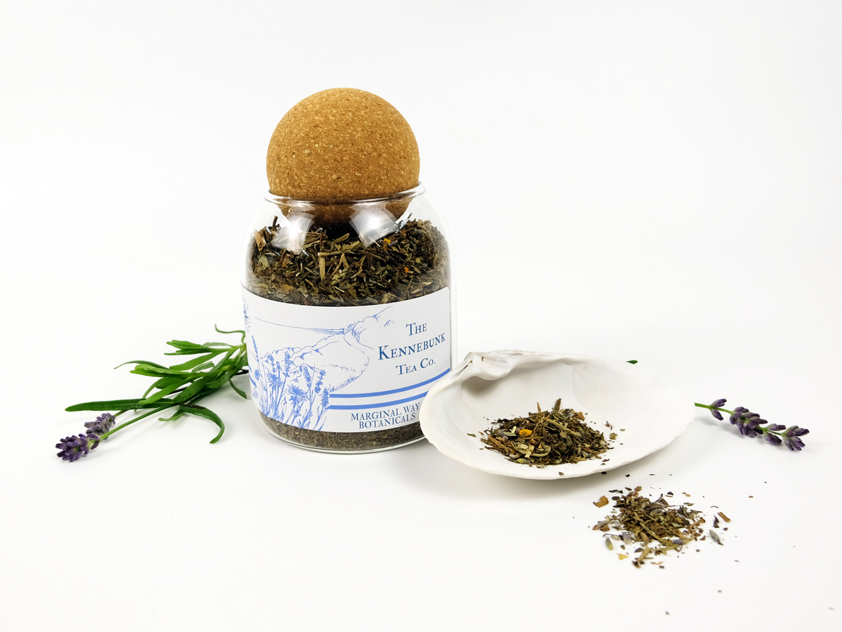 Marginal Way tea jar with a cork lid on a white background, surrounded by dried herbs and lavender.
