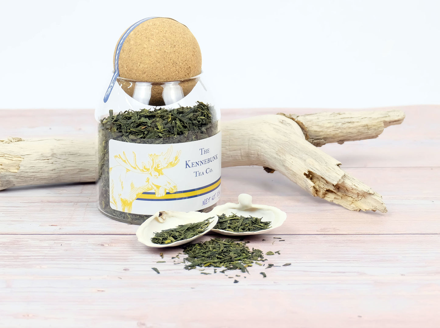 Sencha Green Tea loose leaf tea in a glass jar with two white shells and driftwood beside it