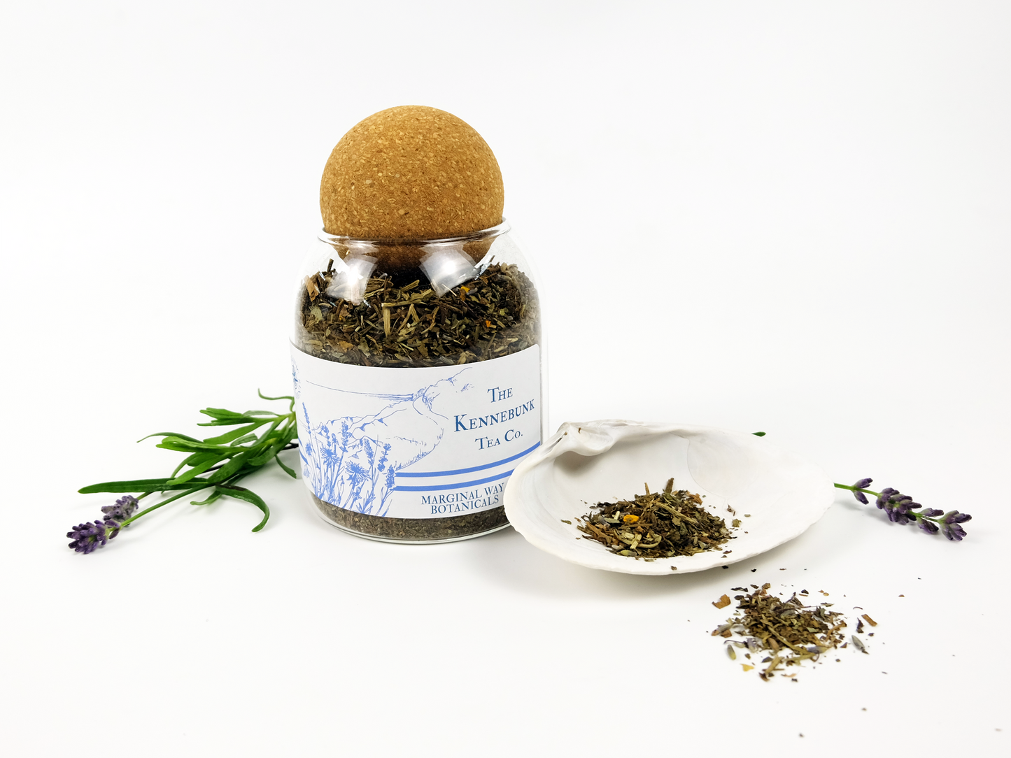 Marginal Way tea jar with a cork lid on a white background, surrounded by dried herbs and lavender.