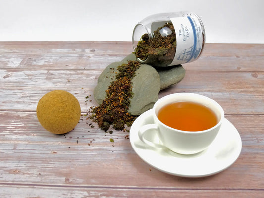 Blueberry Tide loose leaf tea spilling from a glass jar over rocks with a white teacup filled with brewed tea