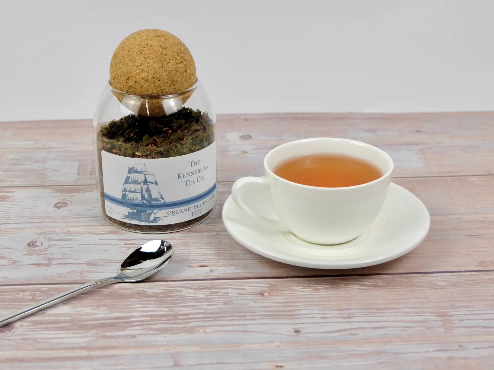Blueberry Tide loose leaf tea in a glass jar with a white teacup and spoon, Clipper Ship label