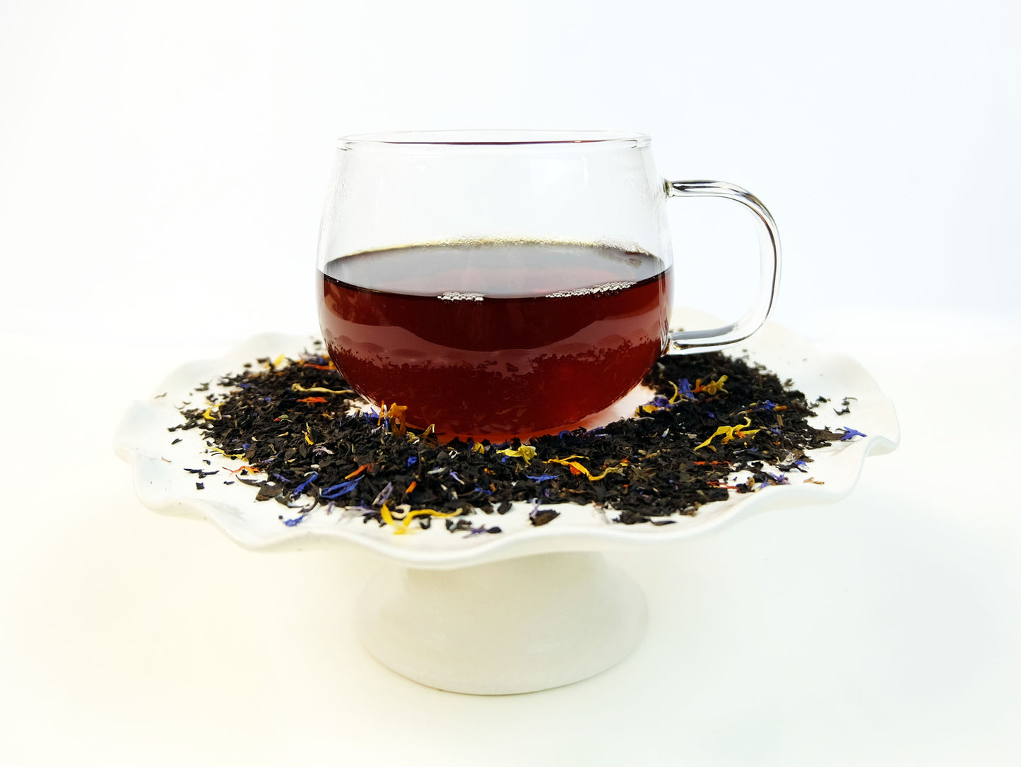 Katahdin Mountain Sunrise Tea brewed in a glass mug with loose leaf tea scattered around, side view