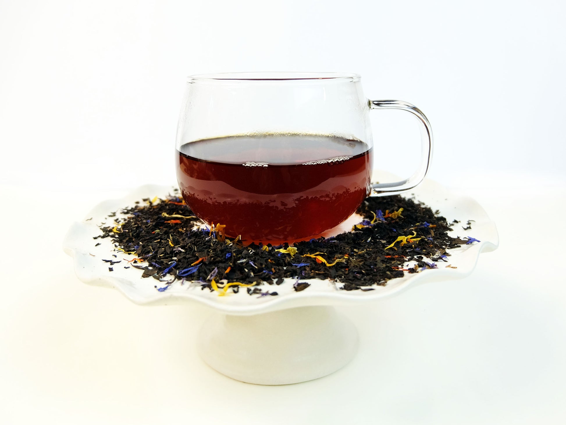 Katahdin Mountain Sunrise Tea brewed in a glass mug with loose leaf tea scattered around, side view