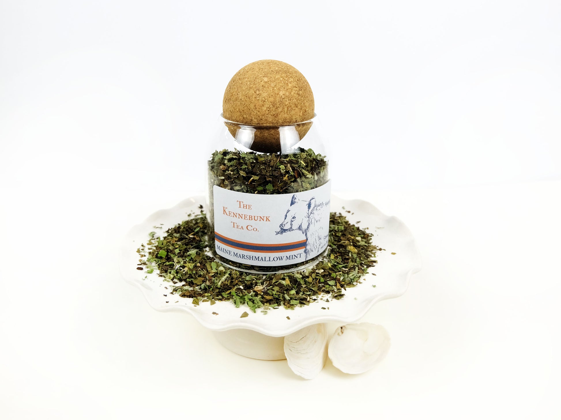 Marshmallow Mint Tea loose leaf tea in a glass jar on a pedestal with loose leaf tea around it