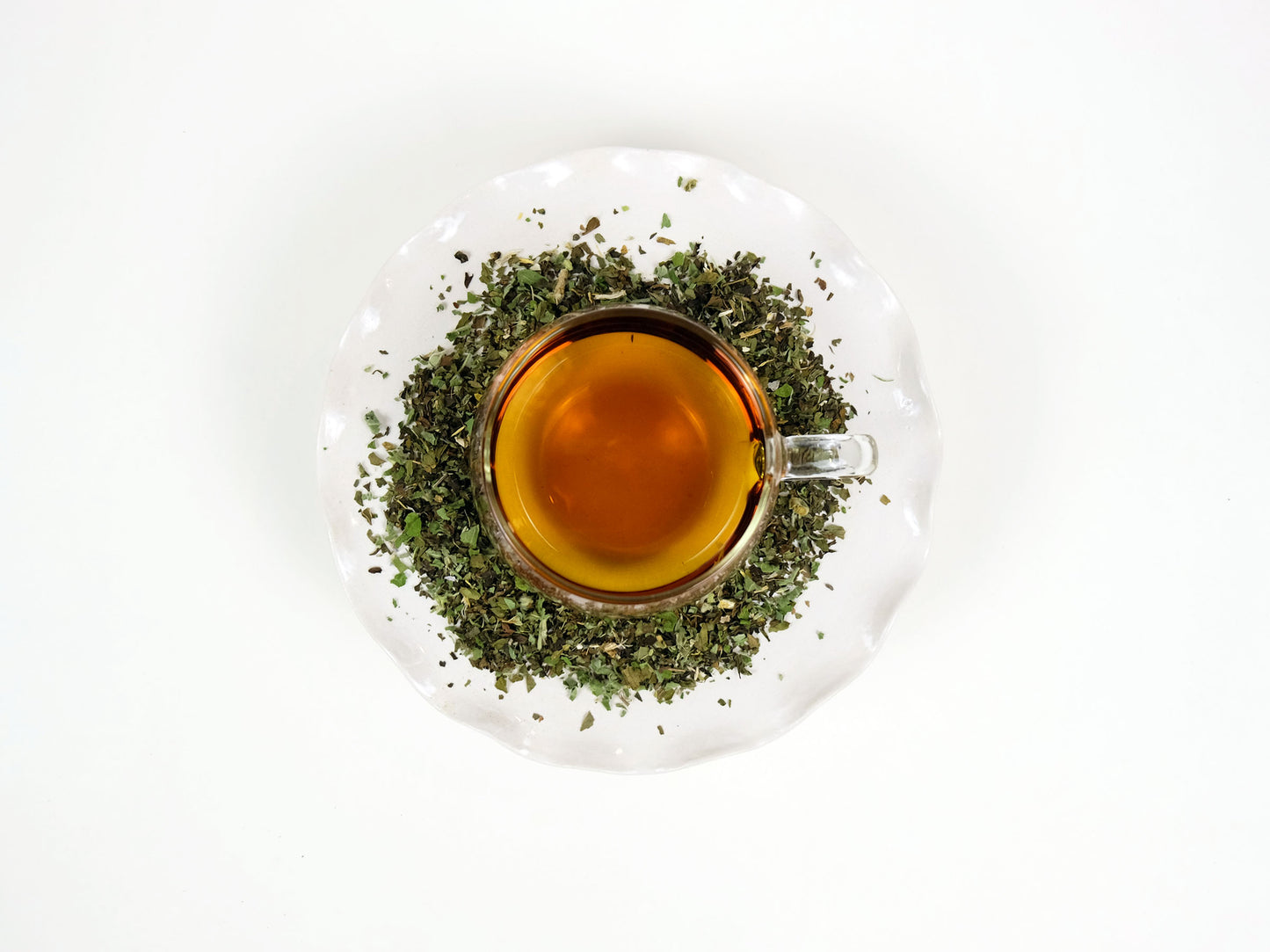 Marshmallow Mint Tea brewed in a glass mug on a pedestal with loose leaf tea around it, top view