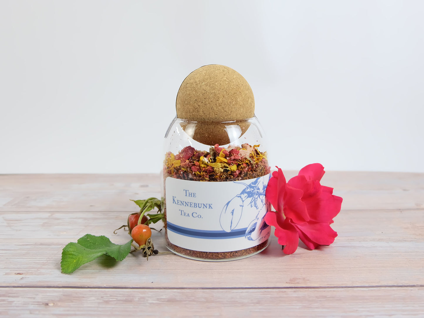 Mother’s Beach Medley Tea loose leaf tea in a glass jar with Lobster Label, with beach rose blossom and rose hips beside it