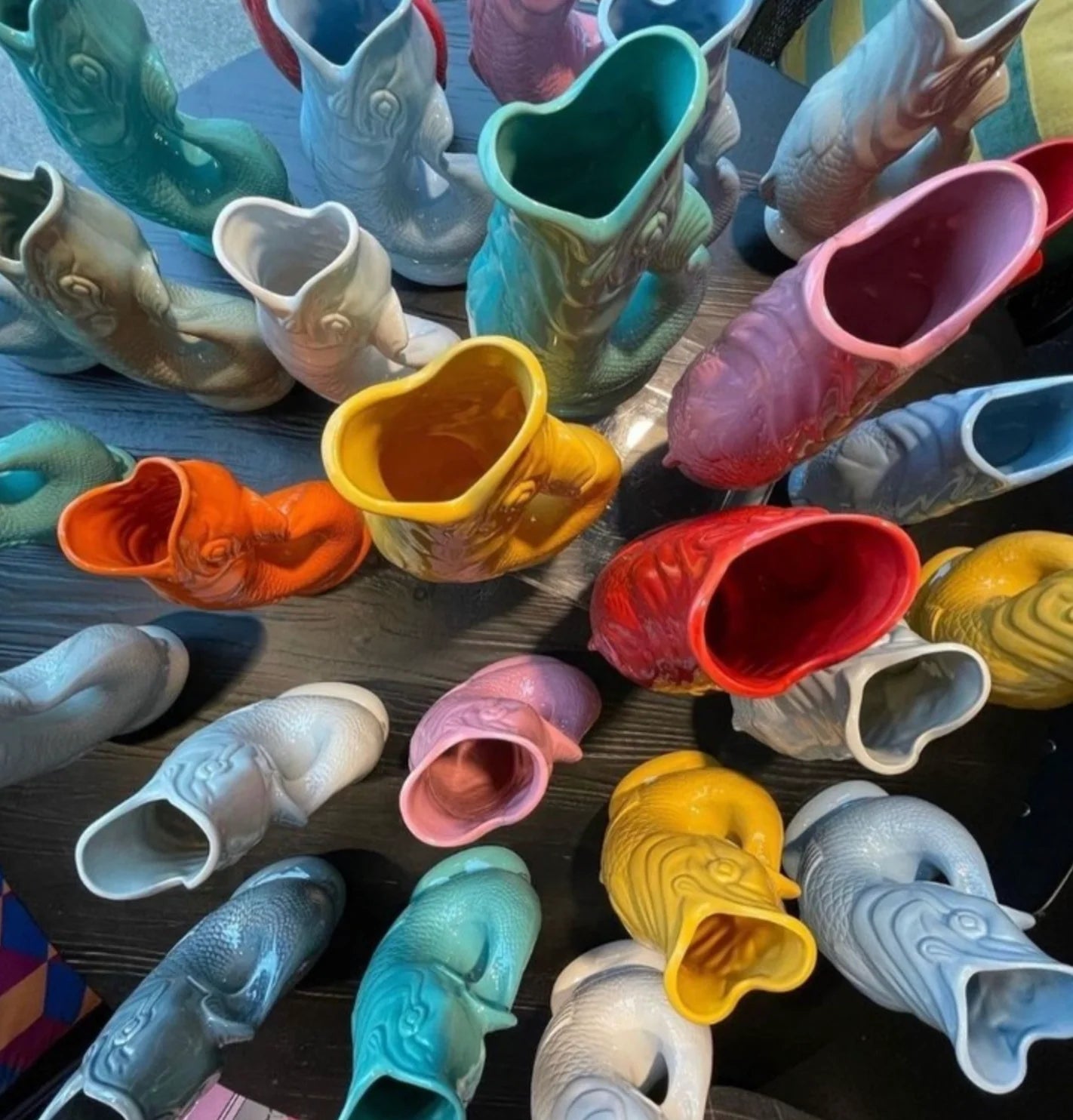 multiple colorful ceramic fish-shaped gluggle jugs on a wooden surface