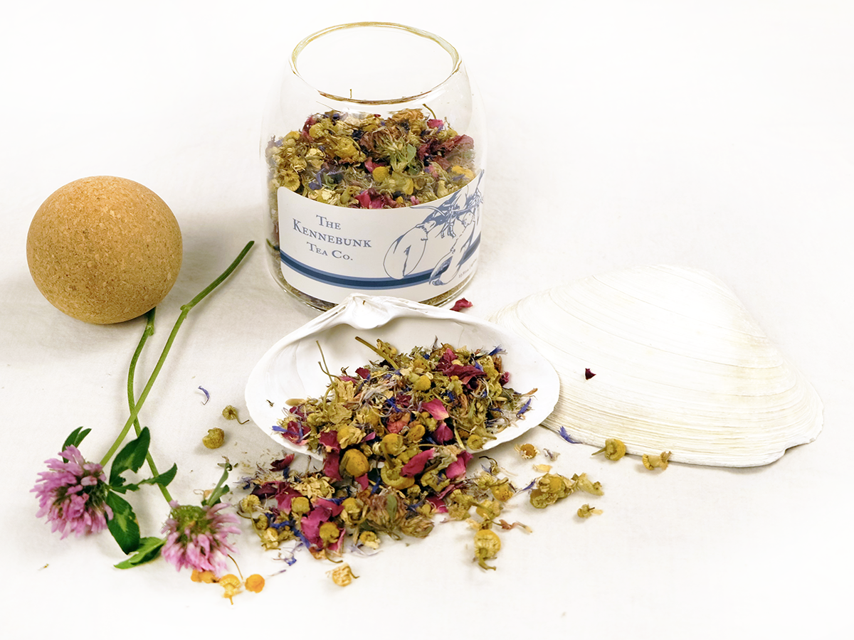 New England Garden Tea loose leaf tea on a white shell with an open glass jar and clover blossoms