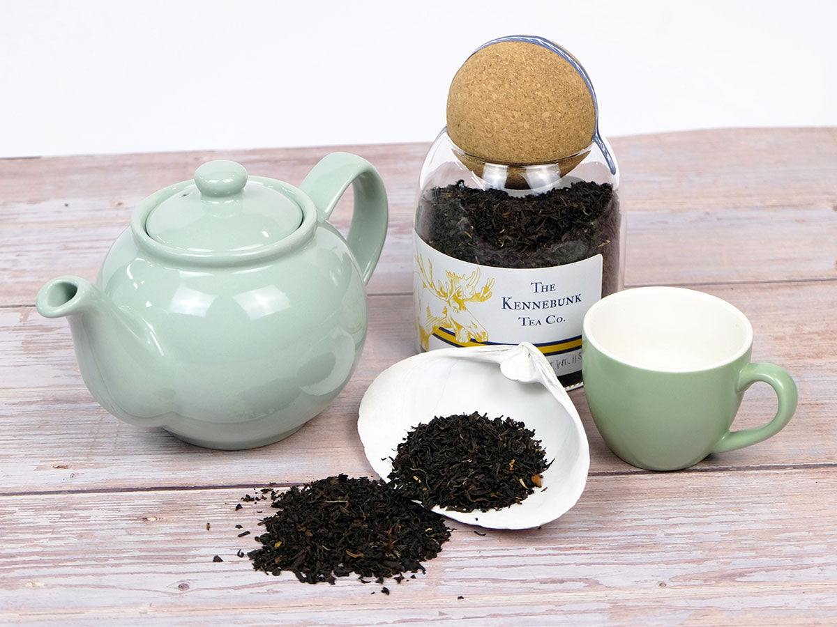 Organic English Breakfast Tea loose leaf tea on a white shell with a glass jar, teapot, and teacup