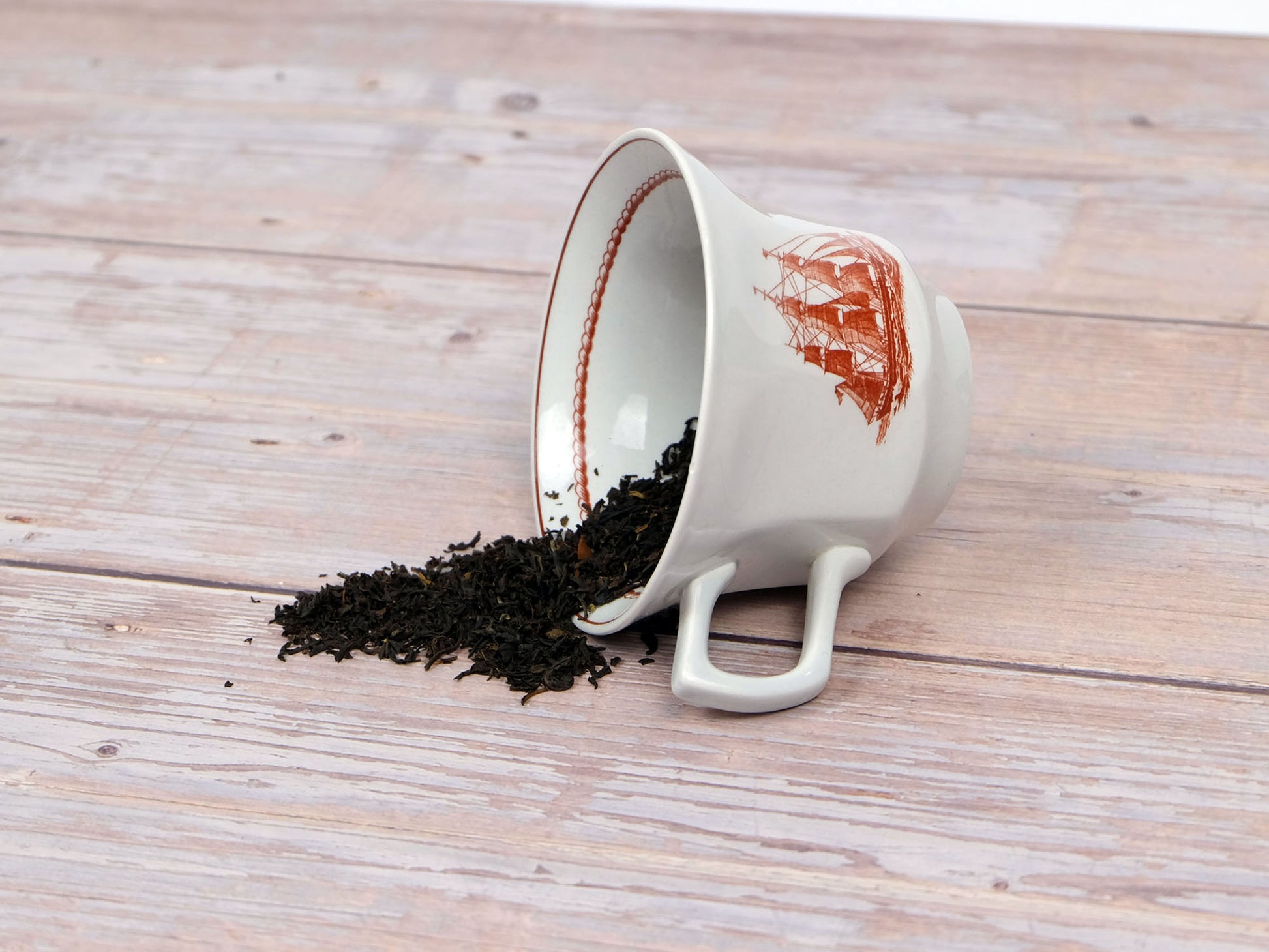 Organic English Breakfast Tea loose leaf tea spilling from a teacup, side view