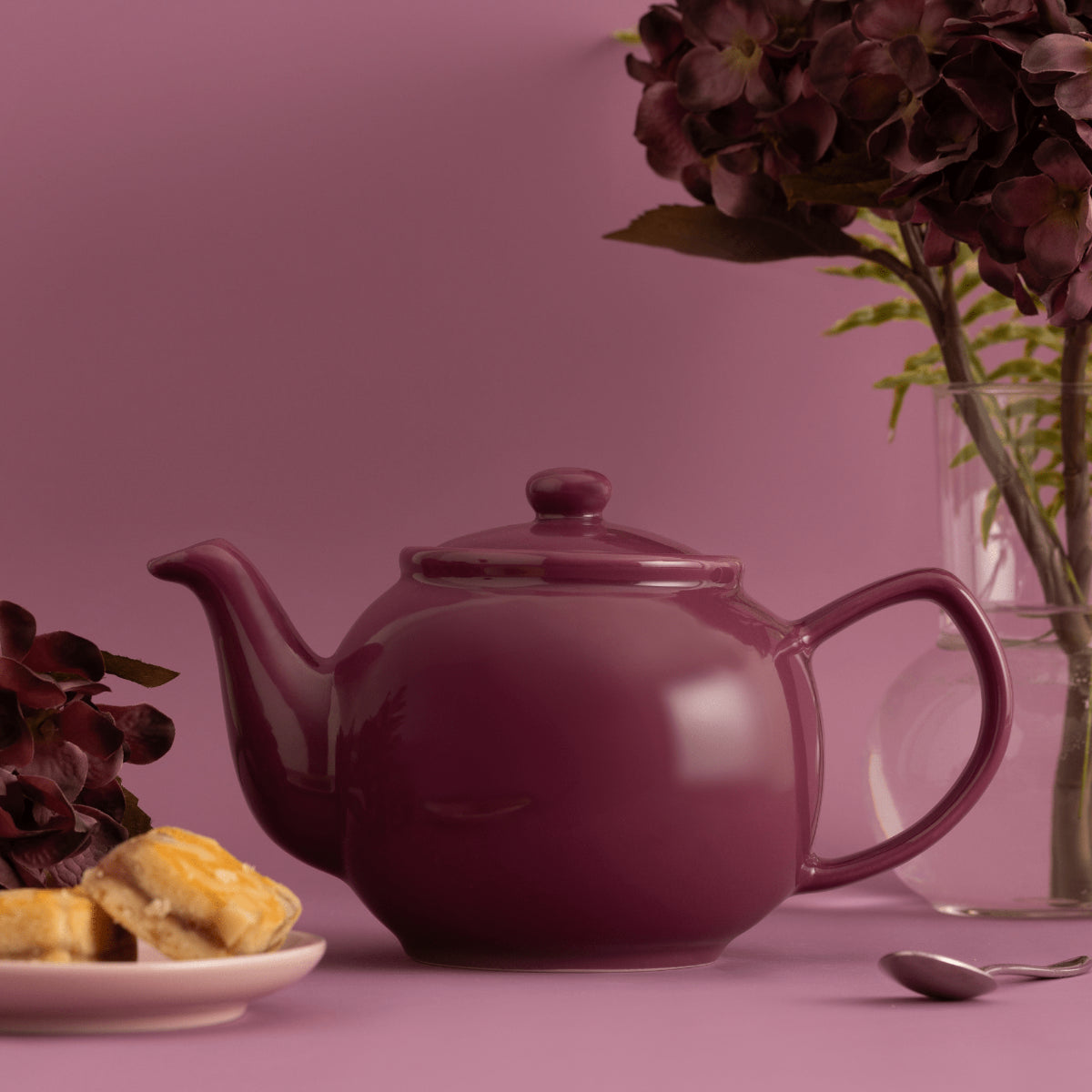 Purple teapot with cookies and a vase on a pink background