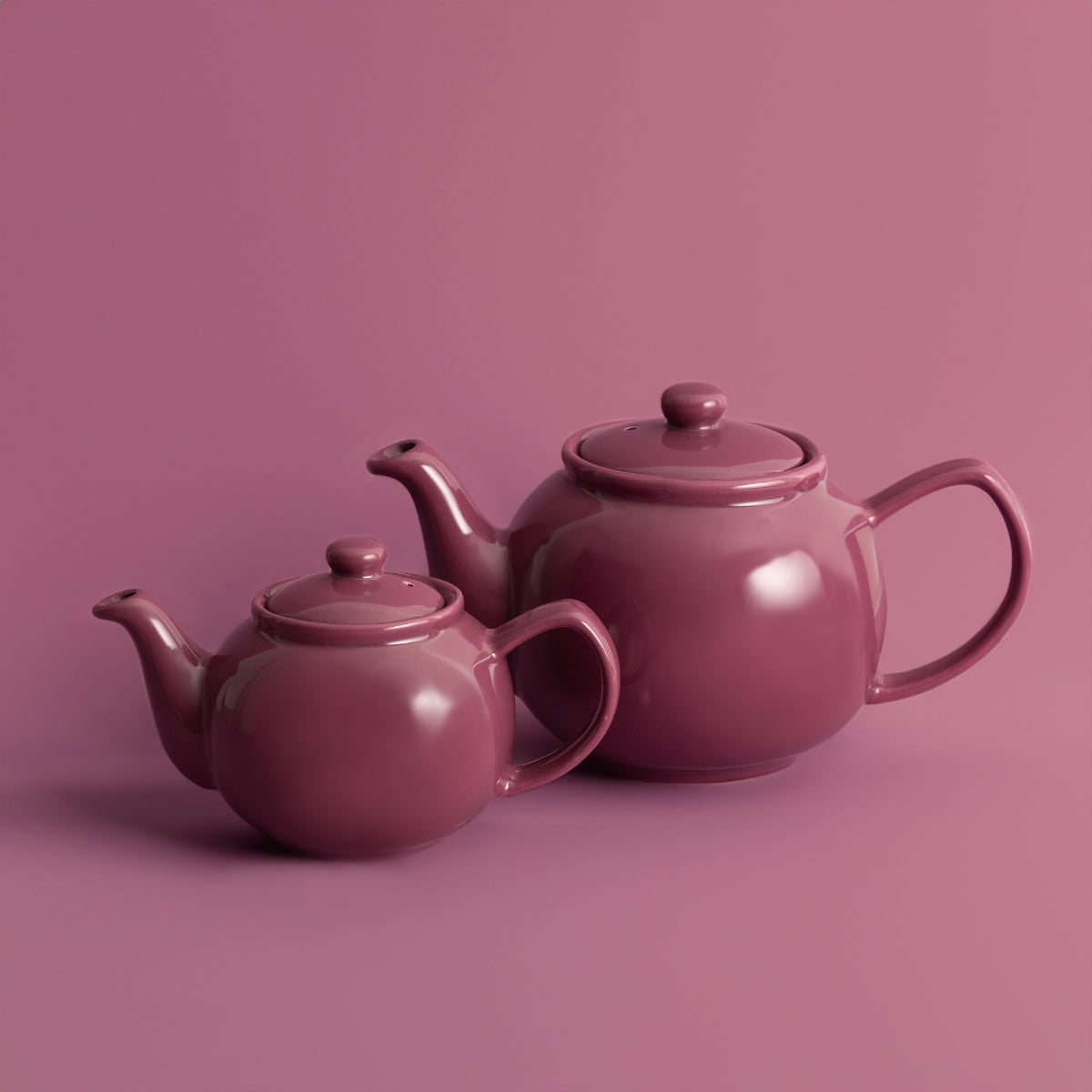 Two magenta teapots on a matching pink background
