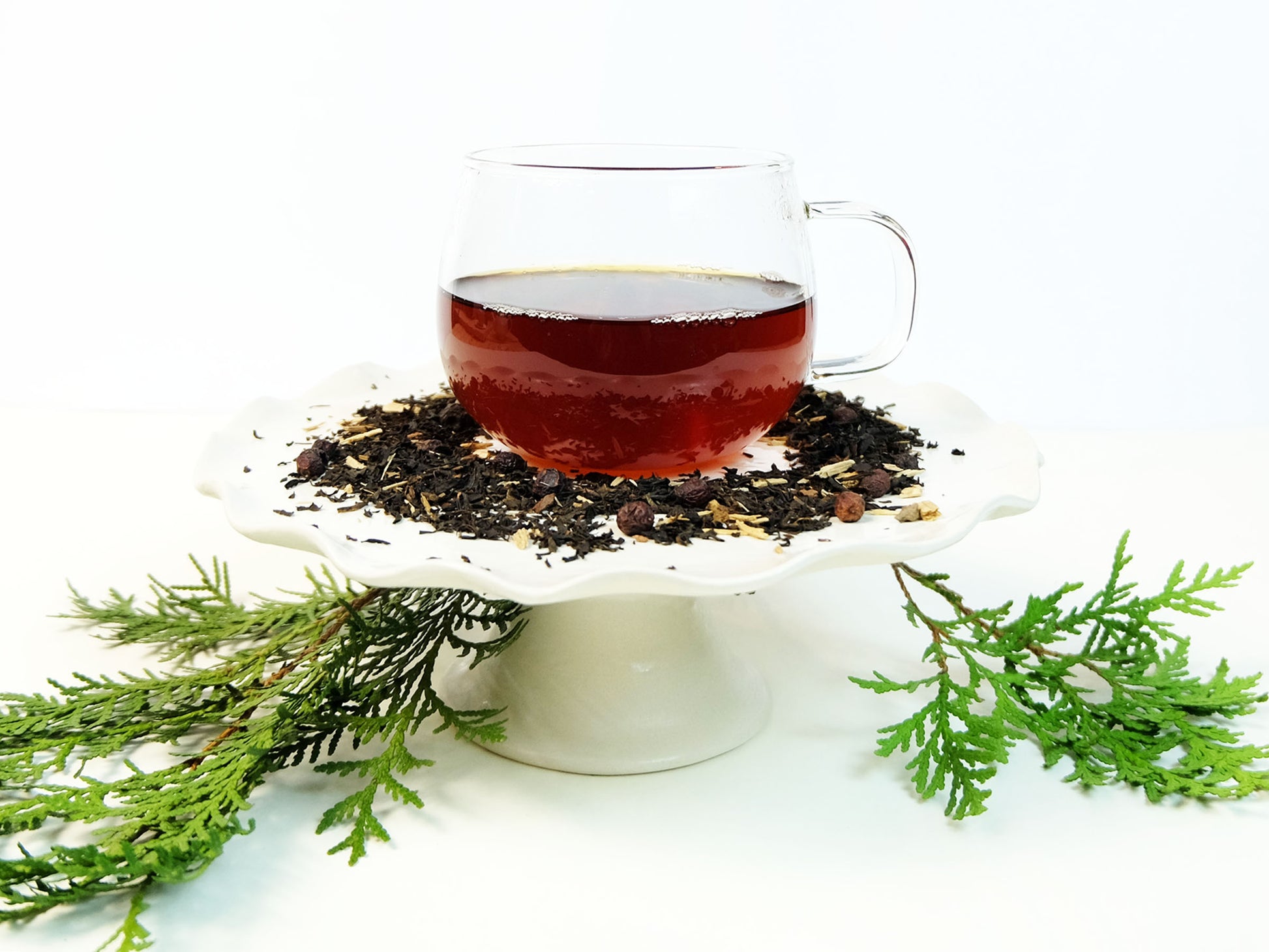 Winter Pine Hawthorn Berry Tea brewed in a glass mug with loose leaf tea and evergreen branch, side view