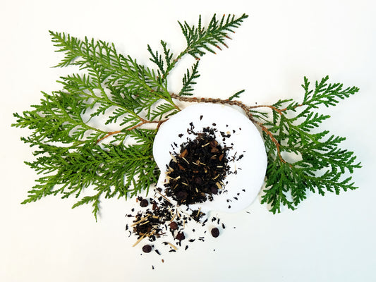 Winter Pine Hawthorn Berry Tea loose leaf tea spilling from a white shell onto an evergreen branch